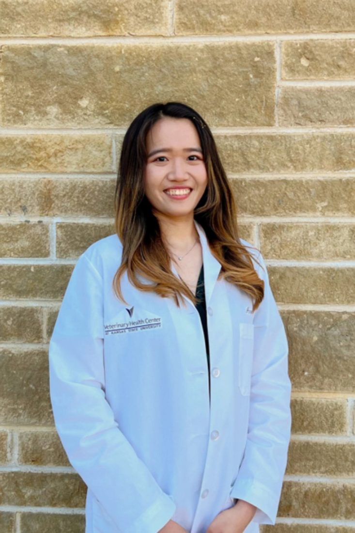 Smiling female veterinarian in white coat standing against a stone wall