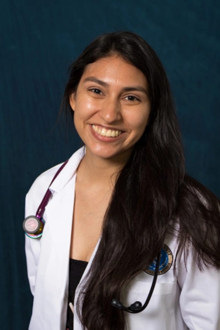 Smiling female veterinarian with stethoscope in white coat against dark blue background